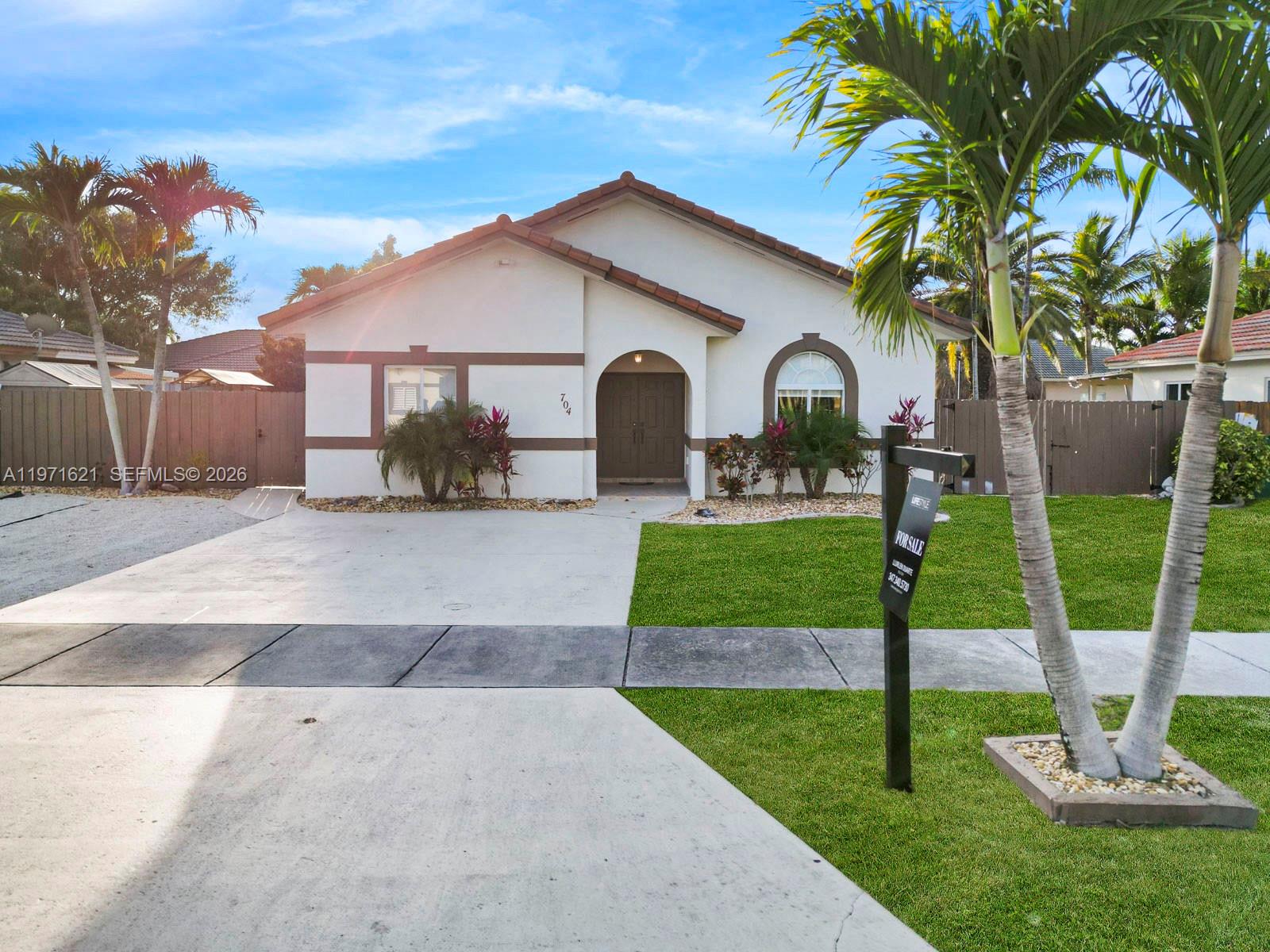 A single-story house with a concrete driveway, a front lawn, and palm trees — 704 SE 14th Pl, Homestead FL 33033, HOMESTEAD, FL