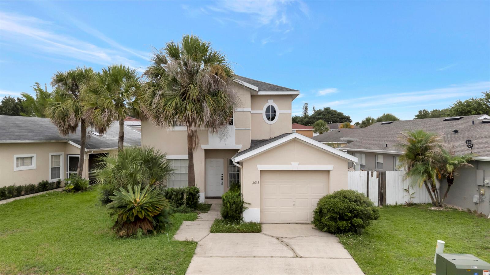 A two-story beige house with a front-facing garage, palm trees, and a concrete driveway — 2613 Spring Hill Drive, Kissimmee FL 34743, KISSIMMEE, FL
