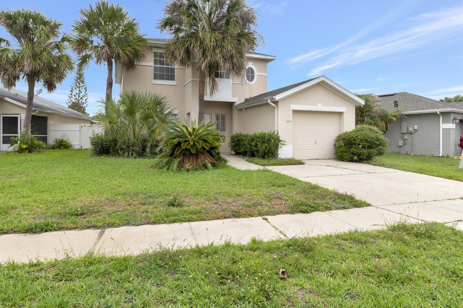 A two-story beige house features a single-car garage, palm trees, and a concrete driveway — 2613 Spring Hill Drive, Kissimmee FL 34743, KISSIMMEE, FL