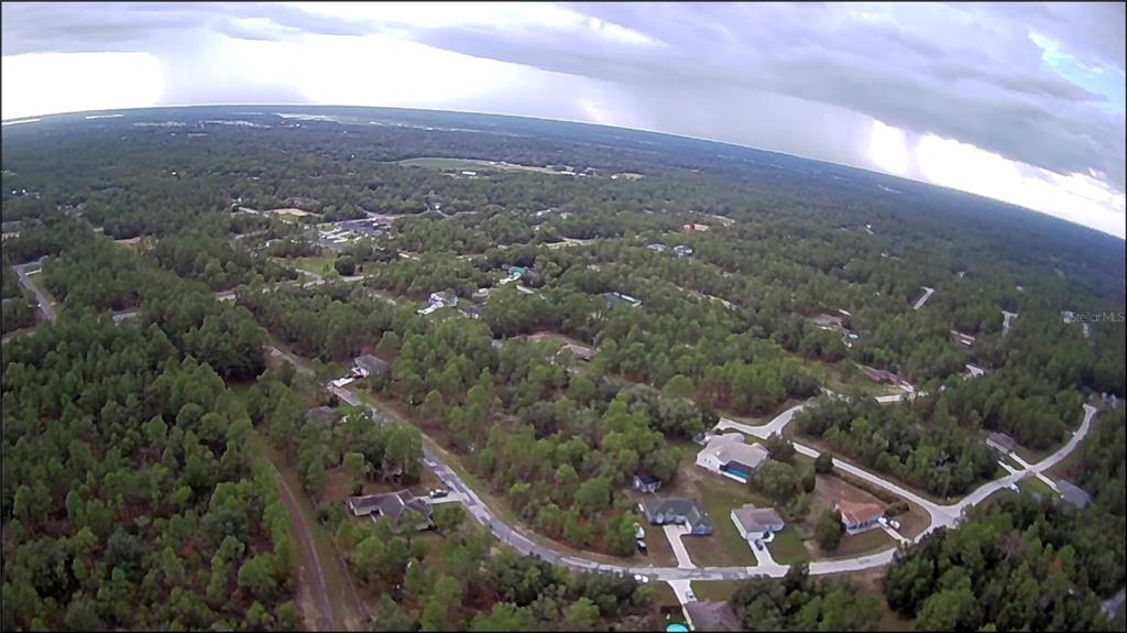 An aerial view shows a residential neighborhood surrounded by dense forest under a cloudy sky — 10522 N ELKCAM BOULEVARD, CITRUS SPRINGS, FL
