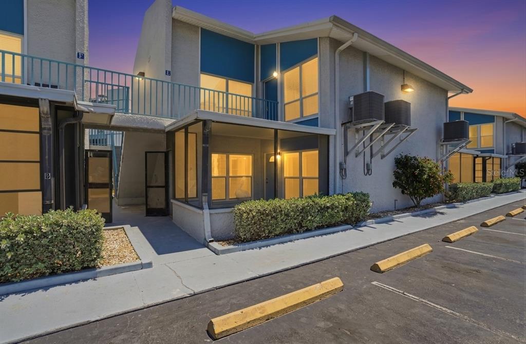 A two-story apartment building exterior features a screened-in porch, blue accents, and parking spaces — 155 MEDALLION BOULEVARD UNIT E, MADEIRA BEACH, FL