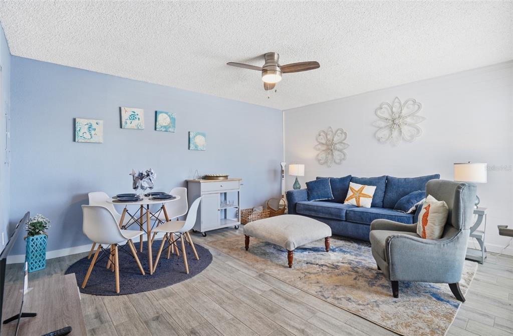 A living room features a blue sofa, a dining set, and light wood-look flooring — 155 MEDALLION BOULEVARD UNIT E, MADEIRA BEACH, FL