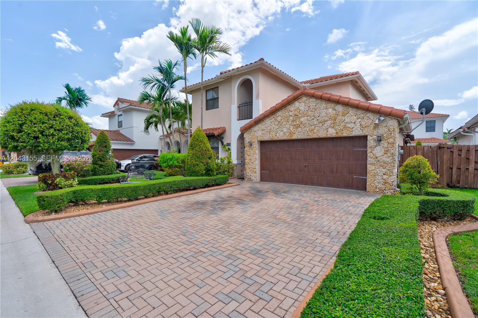 A two-story house features a stone-faced garage, a paved driveway, and manicured hedges — 1016 NW 99th Psge # 1016, Miami FL 33172, MIAMI, FL
