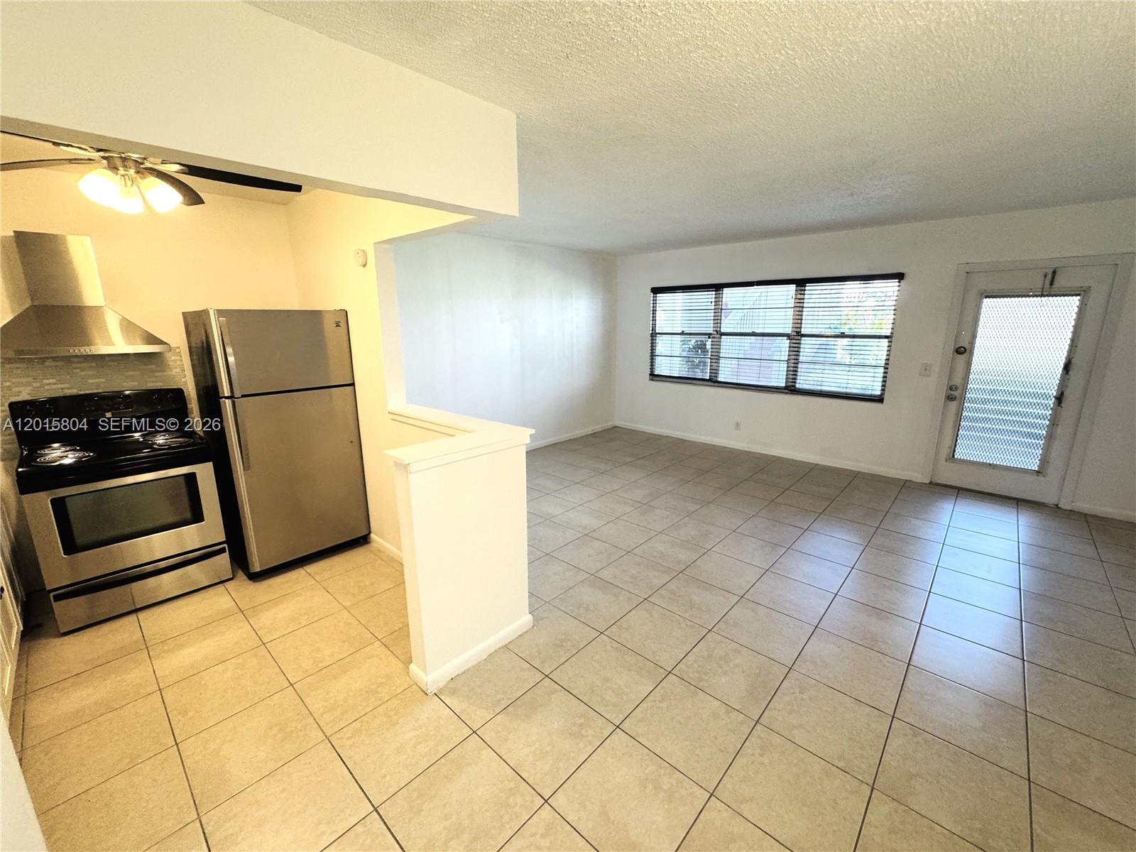 A kitchen with stainless steel appliances opens into a tiled living area with a door — 138 Fanshaw # D, Boca Raton FL 33434, BOCA RATON, FL