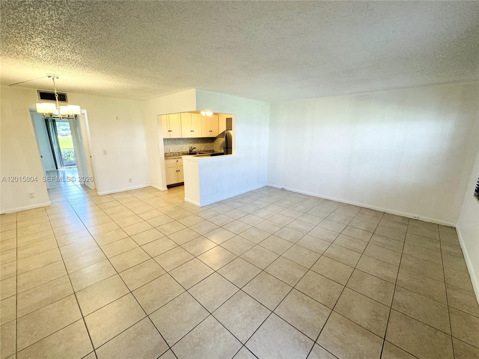 An open-concept living area features beige tile flooring, white walls, and a pass-through kitchen — 138 Fanshaw # D, Boca Raton FL 33434, BOCA RATON, FL