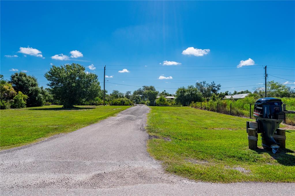 A paved driveway leads through a grassy lot toward trees under a clear blue sky — 30941 TURKEY OAK ROAD, PUNTA GORDA, FL