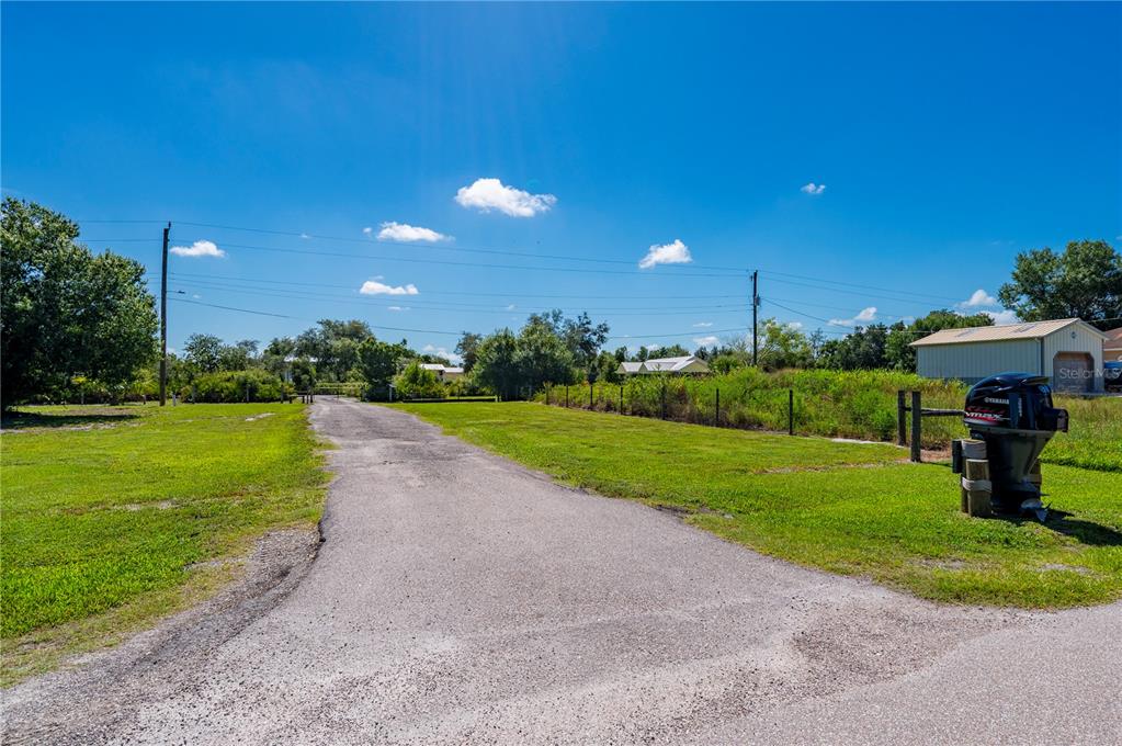A paved driveway leads toward a rural property with a shed and surrounding grassy fields — 30941 TURKEY OAK ROAD, PUNTA GORDA, FL