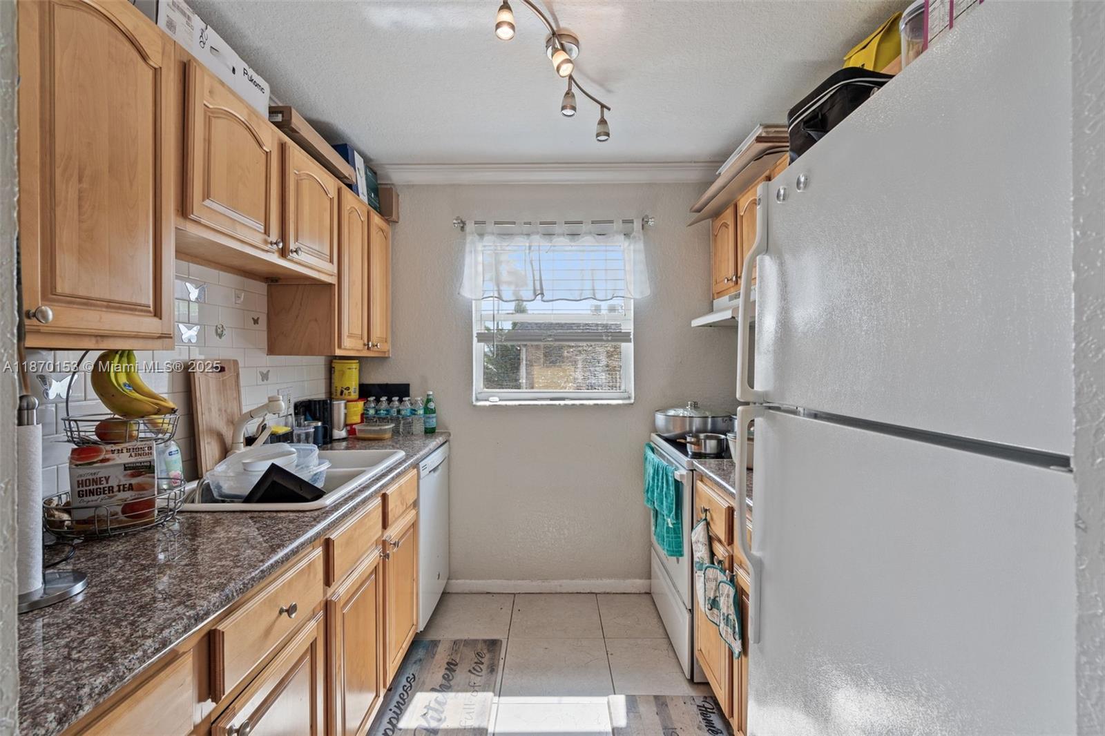 A galley kitchen features light wood cabinets, granite countertops, a white refrigerator, and a window — 200 Croton Ave # 111, Lantana FL 33462, LANTANA, FL