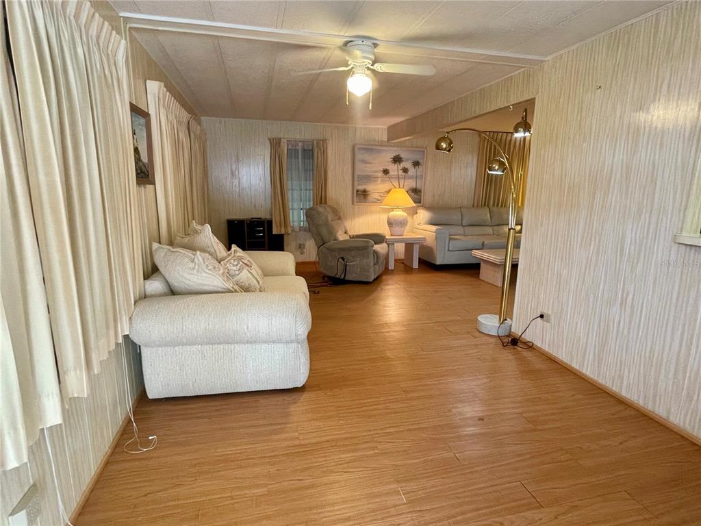 A living room features wood-look flooring, wood-paneled walls, a ceiling fan, and beige furniture — 5619 BAYSHORE ROAD UNIT 161, PALMETTO, FL