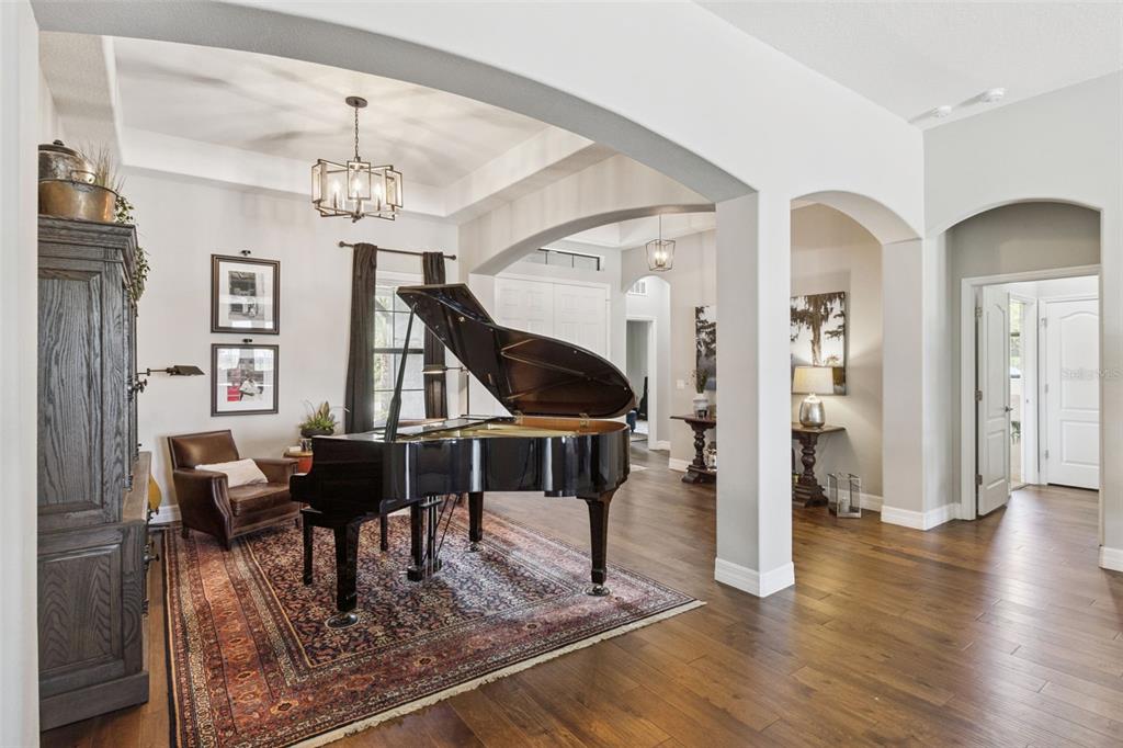 A grand piano sits on a patterned rug in a living room with arched openings — 2590 LAKE MANOR DRIVE, LAND O LAKES, FL