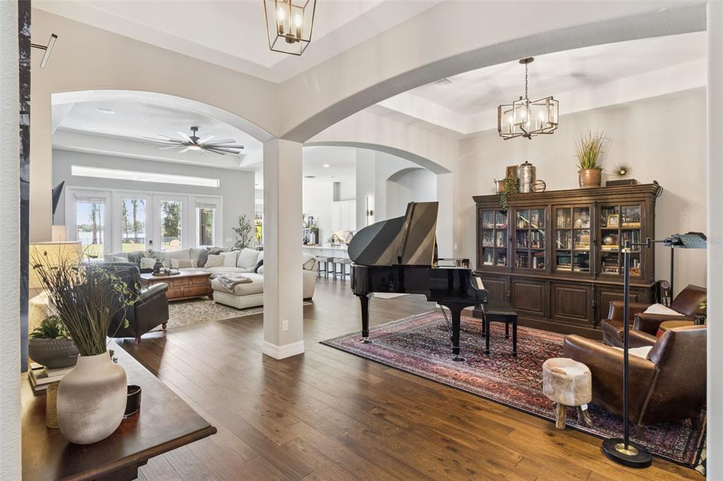 A grand piano sits on a patterned rug in an open-concept living area with hardwood floors — 2590 LAKE MANOR DRIVE, LAND O LAKES, FL