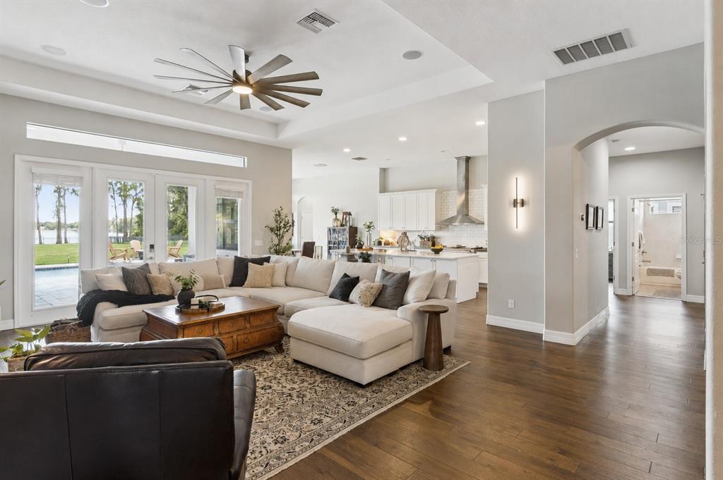 A spacious open-concept living room features a large sectional sofa, hardwood floors, and a kitchen — 2590 LAKE MANOR DRIVE, LAND O LAKES, FL