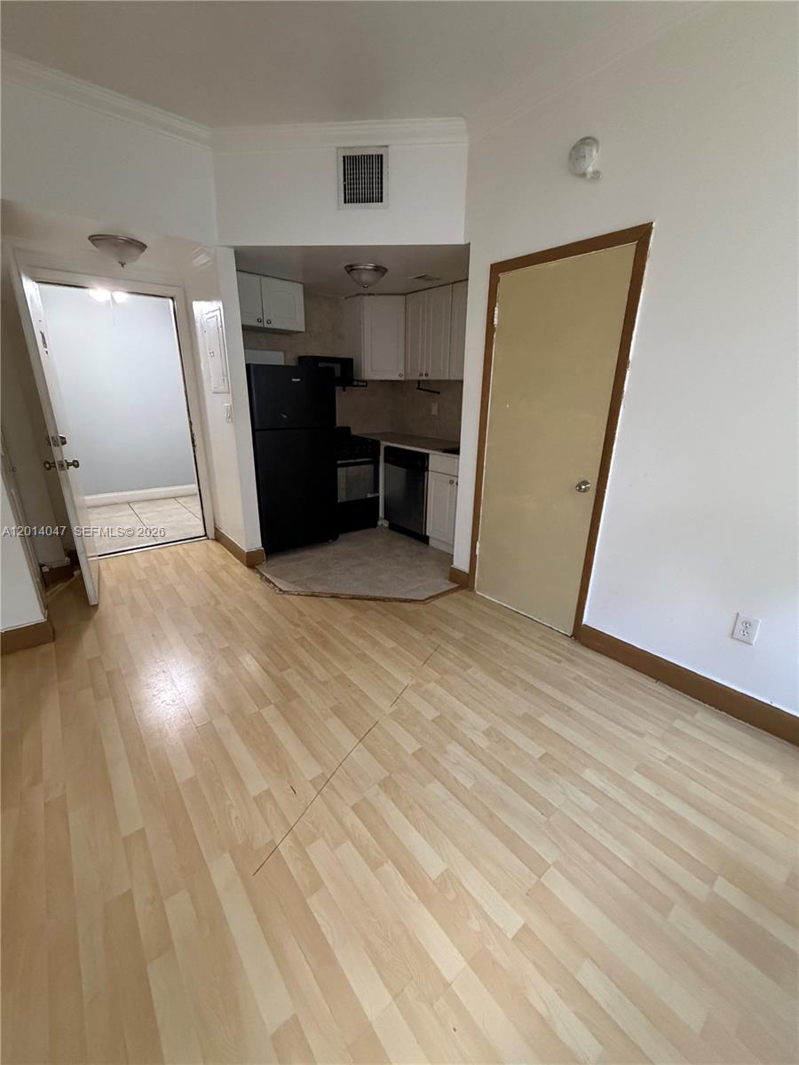 A small kitchen with white cabinets and black appliances sits adjacent to a living area — 1342 Drexel Ave # 205, Miami Beach FL 33139, MIAMI BEACH, FL