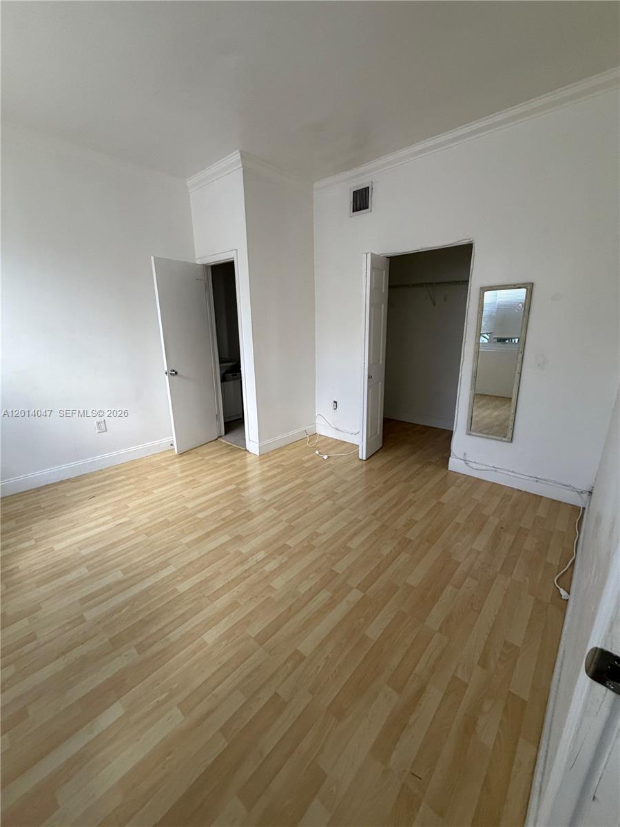 An empty room features light wood-look flooring, white walls, two doorways, and a wall mirror — 1342 Drexel Ave # 205, Miami Beach FL 33139, MIAMI BEACH, FL