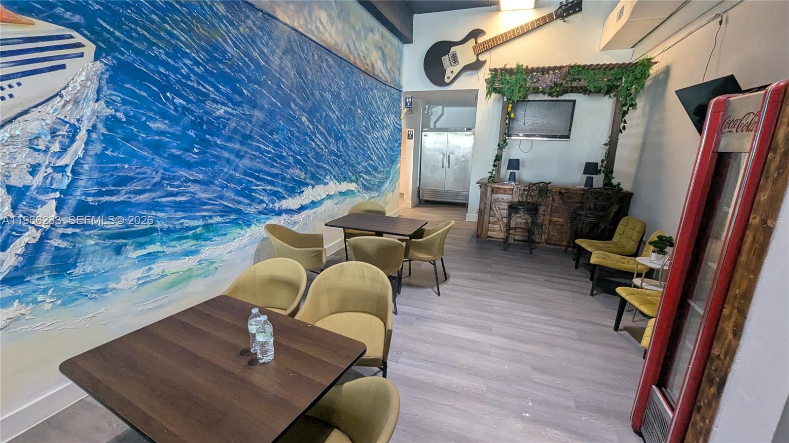 A dining area features a large ocean mural, a wall-mounted guitar, and several tables — 1020 71st St # 106, Miami Beach FL 33141, MIAMI BEACH, FL