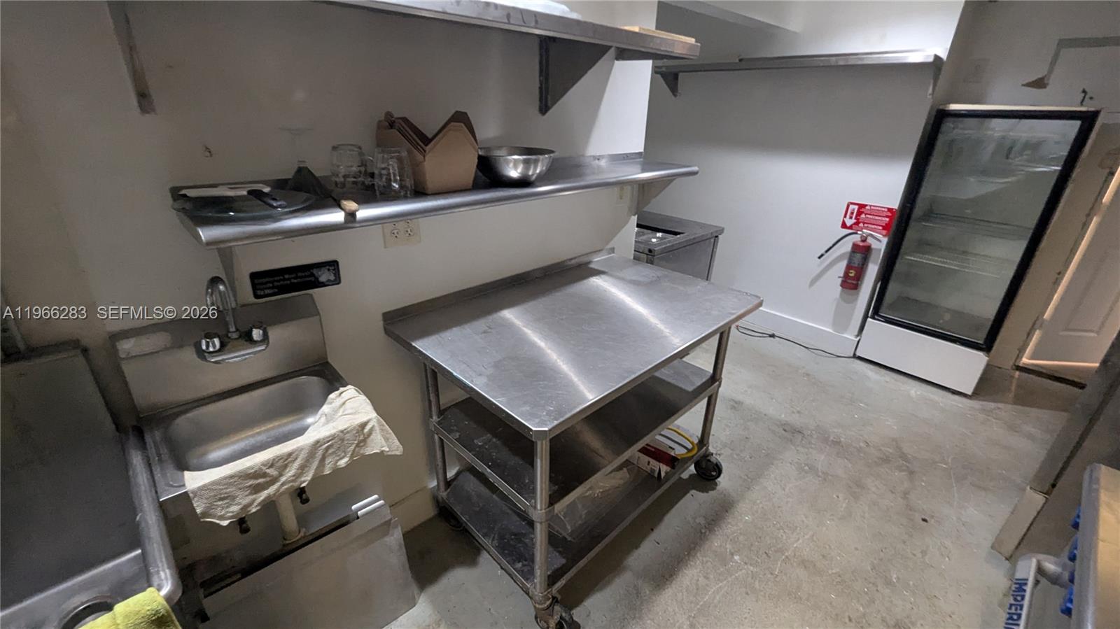 A commercial kitchen features a stainless steel prep table, a sink, and a glass-door refrigerator — 1020 71st St # 106, Miami Beach FL 33141, MIAMI BEACH, FL