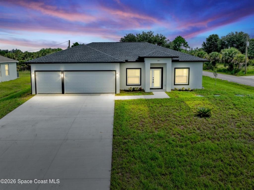 A single-story house with a two-car garage and a concrete driveway at dusk — 601 YARDLEY STREET SW, PALM BAY, FL