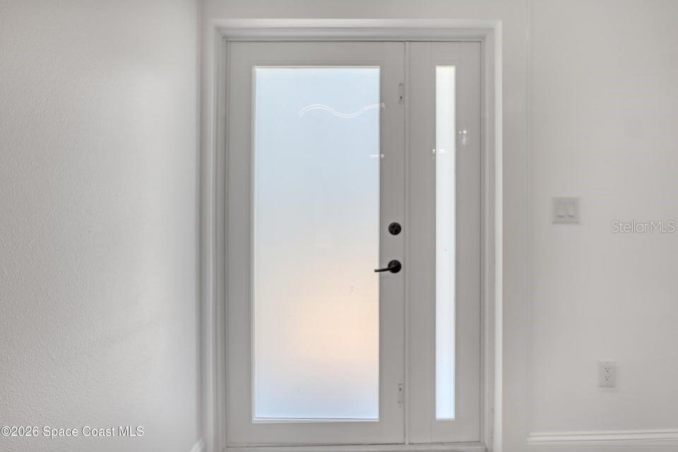 A white front door with a frosted glass panel and a matching side light — 601 YARDLEY STREET SW, PALM BAY, FL