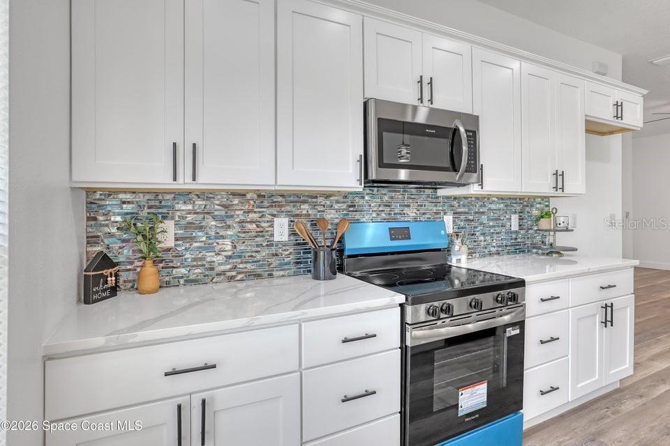 A kitchen features white cabinets, a marble-look countertop, and a blue-toned glass tile backsplash — 601 YARDLEY STREET SW, PALM BAY, FL