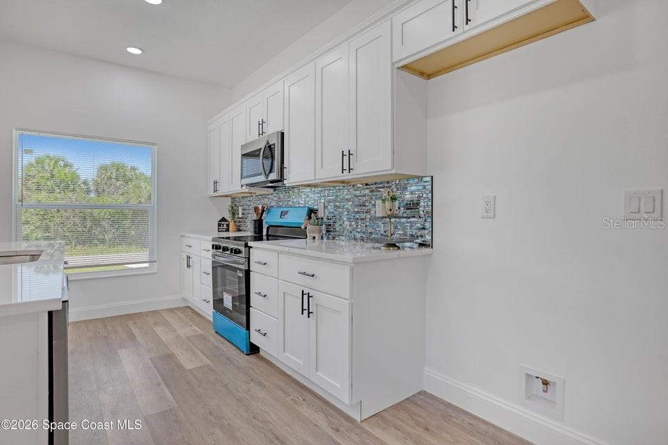 A kitchen features white cabinets, a blue mosaic tile backsplash, and stainless steel appliances — 601 YARDLEY STREET SW, PALM BAY, FL