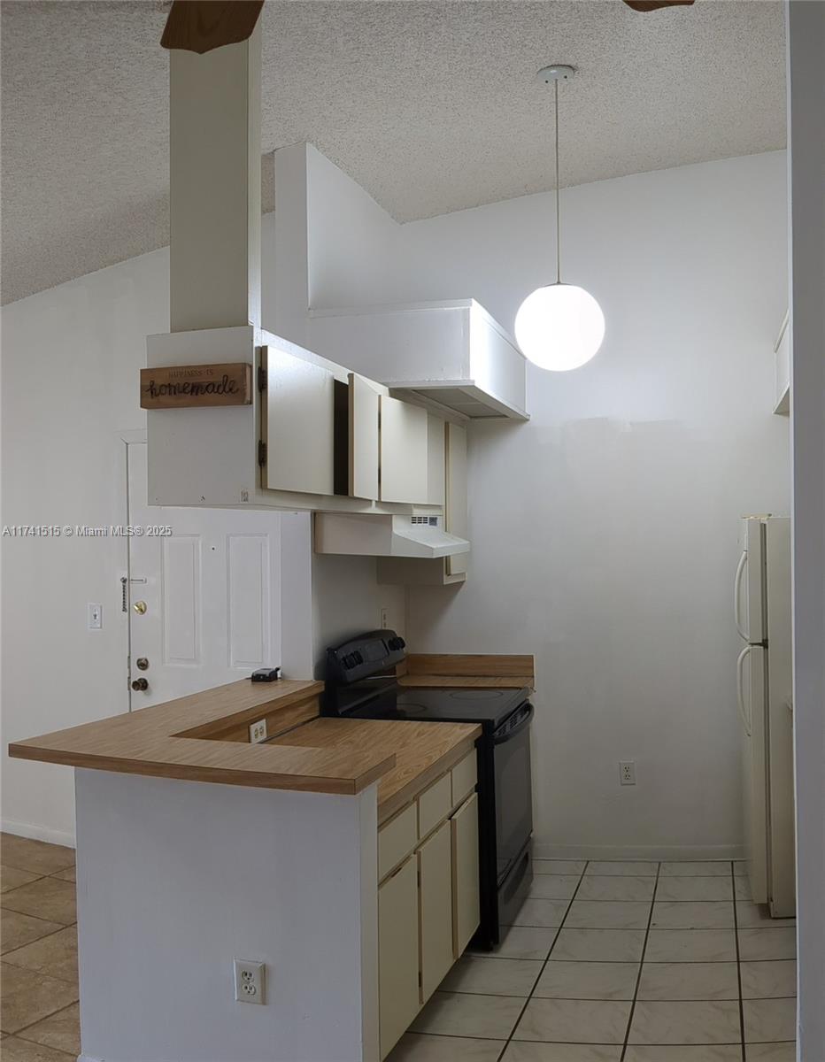 A kitchen features white cabinets, a black stove, a wooden countertop, and a globe pendant light — 917 NE 199th St # 206, Miami FL 33179, MIAMI, FL
