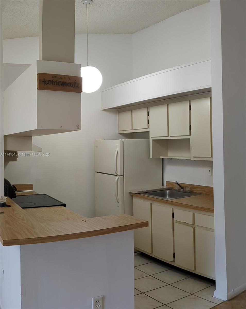 A kitchen features white cabinets, a wood-look countertop, a white refrigerator, and a cooktop — 917 NE 199th St # 206, Miami FL 33179, MIAMI, FL