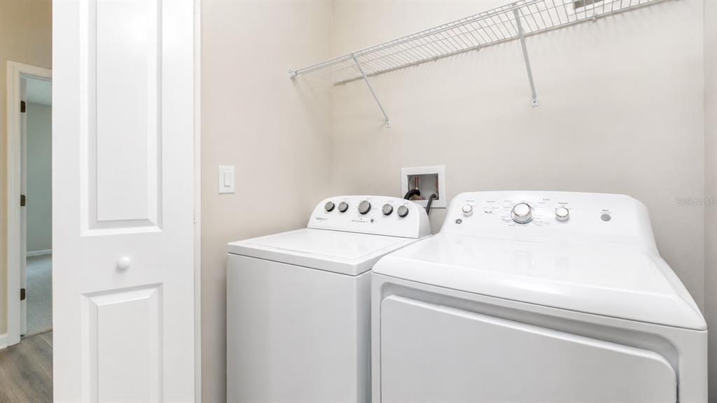 A laundry room features a white washer and dryer beneath a wire storage shelf — 4836 TRIBUTE TRAIL, KISSIMMEE, FL