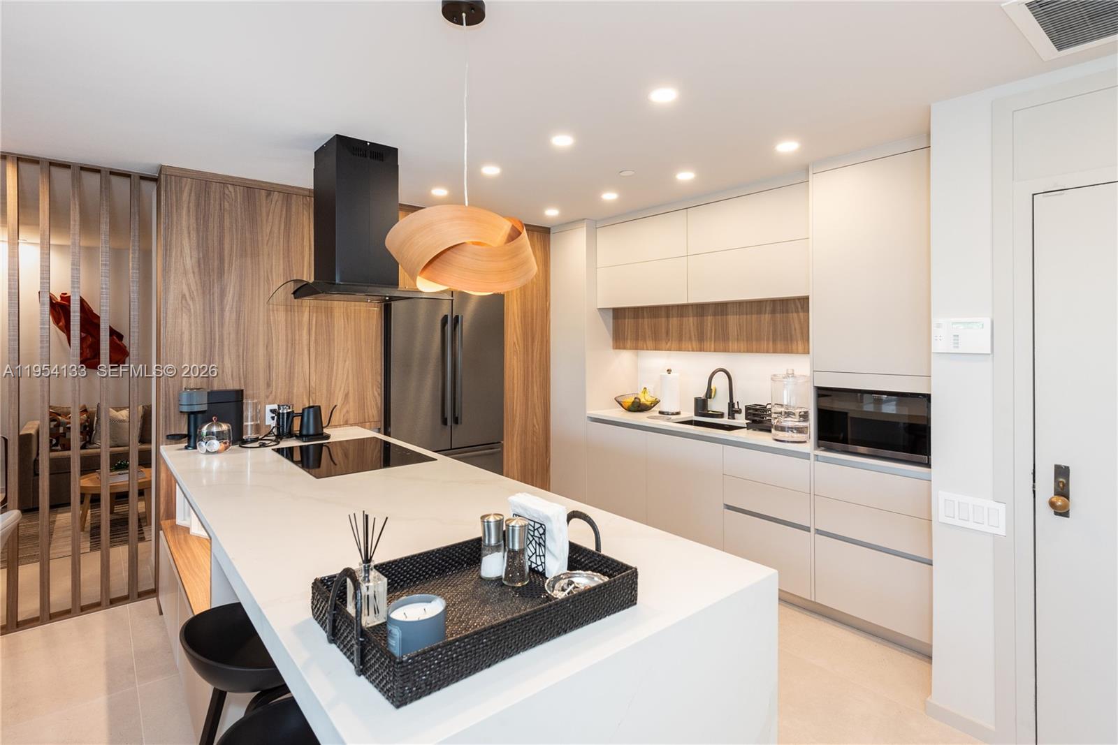 A modern kitchen features a white island, light cabinetry, wood paneling, and a sculptural pendant light — 251 Crandon Blvd # 306, Key Biscayne FL 33149, KEY BISCAYNE, FL