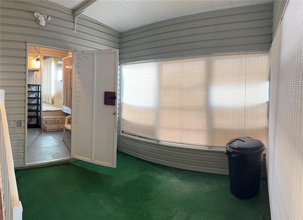 A covered porch with green carpet, vinyl siding, and a large window with bamboo shades — 3301 ALT 19 UNIT 167, DUNEDIN, FL