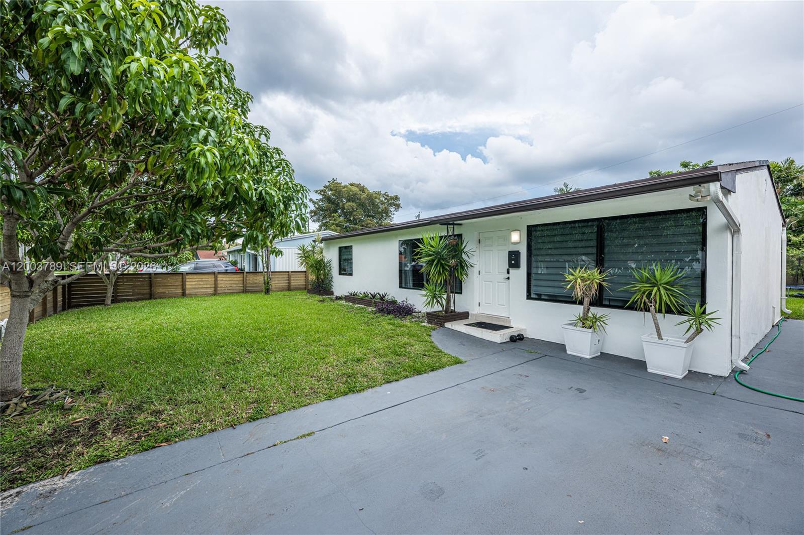 A white single-story house features a front lawn, a gray driveway, and potted plants — 906 NE 6th St # 0, Hallandale Beach FL 33009, HALLANDALE BEACH, FL