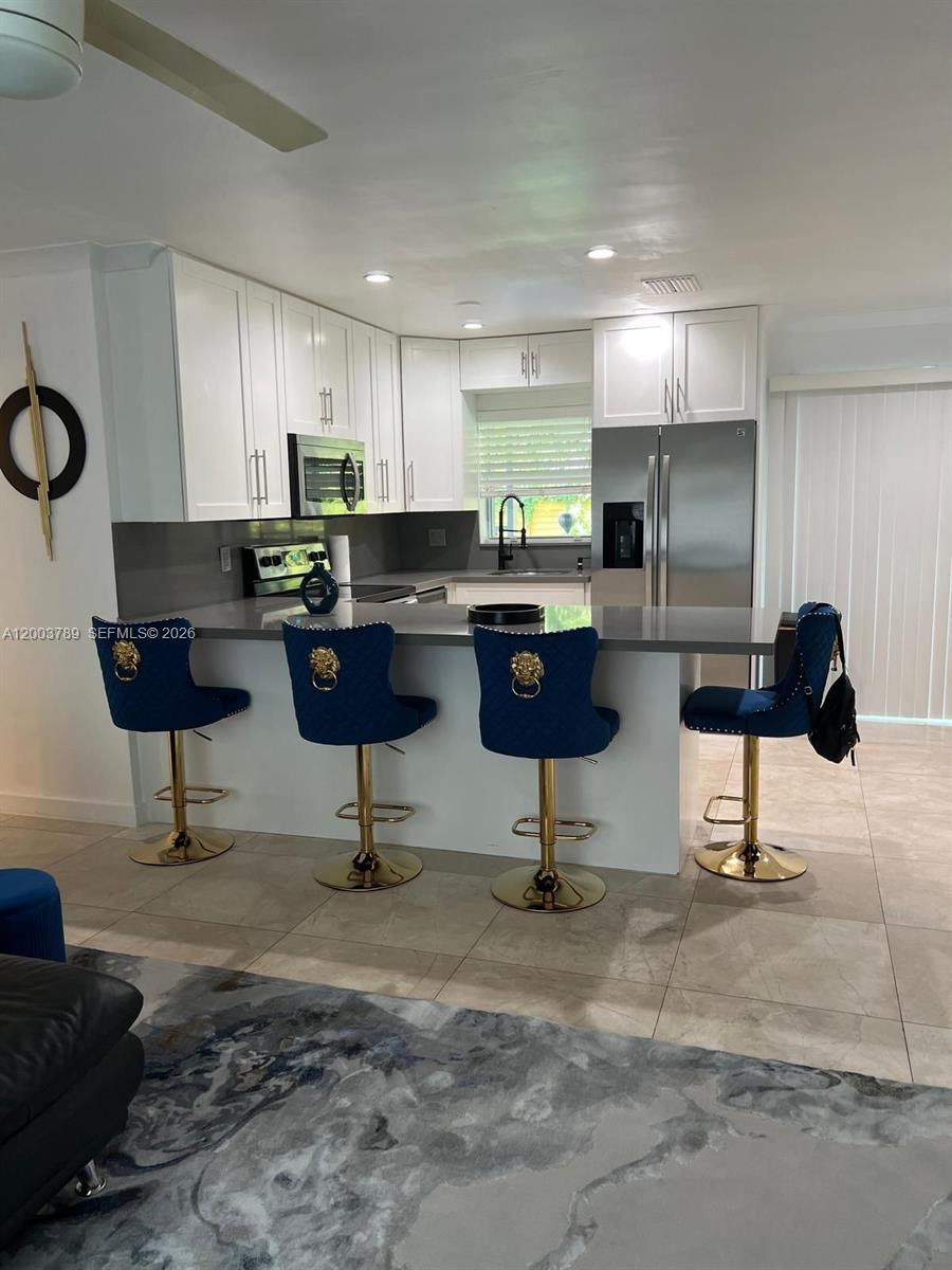 A modern kitchen features white cabinetry, stainless steel appliances, and four blue velvet barstools — 906 NE 6th St # 0, Hallandale Beach FL 33009, HALLANDALE BEACH, FL