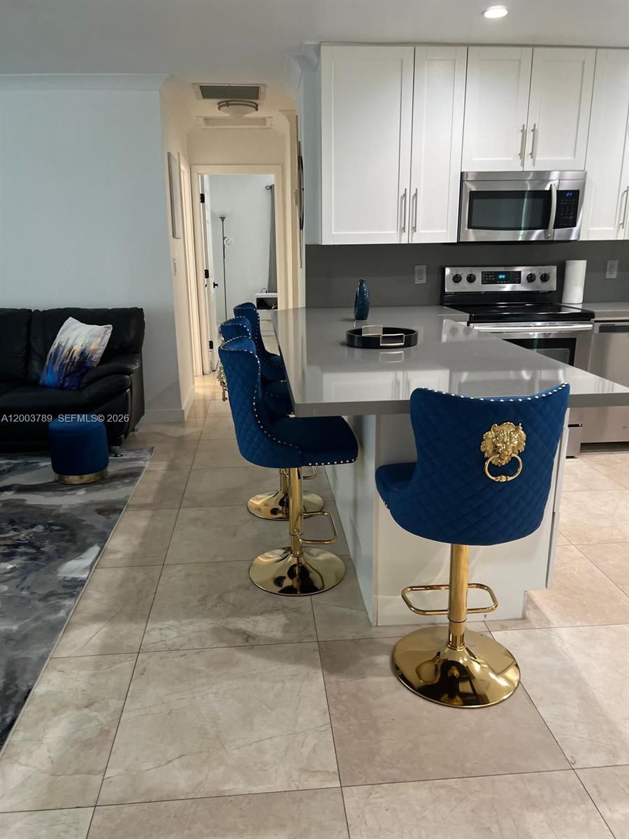 A kitchen features white cabinets, a gray island, and blue bar stools with gold accents — 906 NE 6th St # 0, Hallandale Beach FL 33009, HALLANDALE BEACH, FL