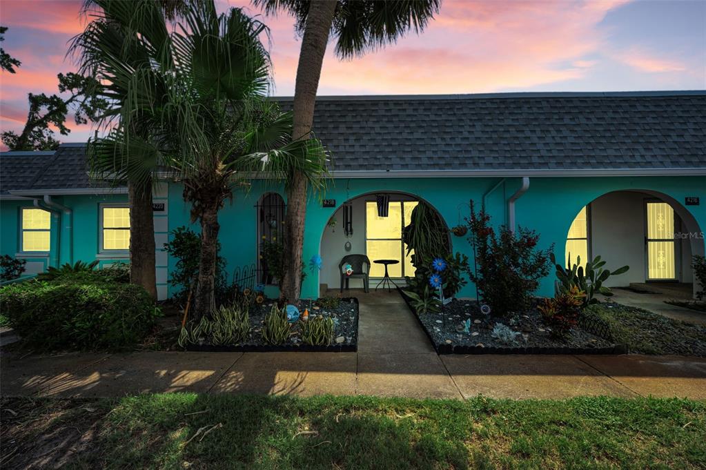 The exterior of a teal-colored building features arched entryways, a palm tree, and landscaped gardens — 4218 TERRAPIN PLACE UNIT D, NEW PORT RICHEY, FL