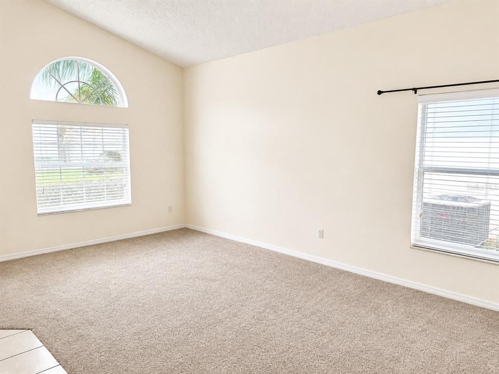 An empty room features beige carpet, cream-colored walls, a single window with blinds, and vaulted ceilings — 16647 FRESH MEADOW DRIVE, CLERMONT, FL