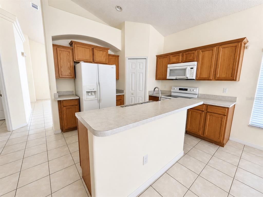 A spacious, empty living room features light-colored tile flooring, a vaulted ceiling, and mirrored walls — 16647 FRESH MEADOW DRIVE, CLERMONT, FL