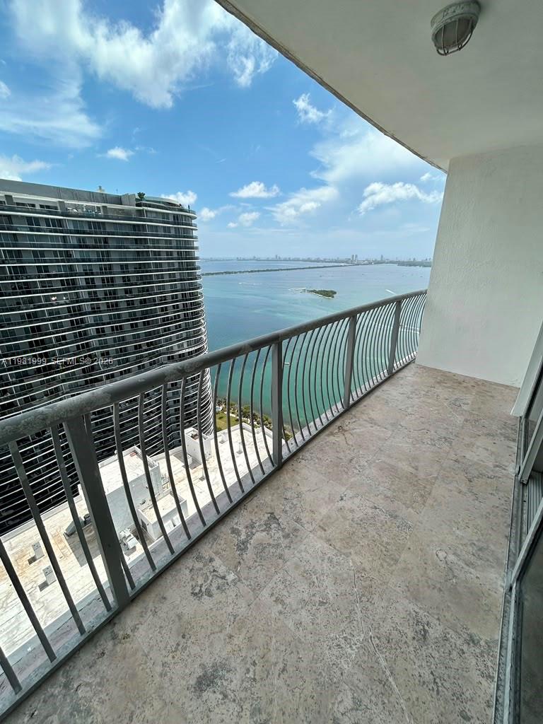 A balcony with stone flooring overlooks a large body of water and a neighboring skyscraper — 1750 N Bayshore Dr # 5307, Miami FL 33132, MIAMI, FL