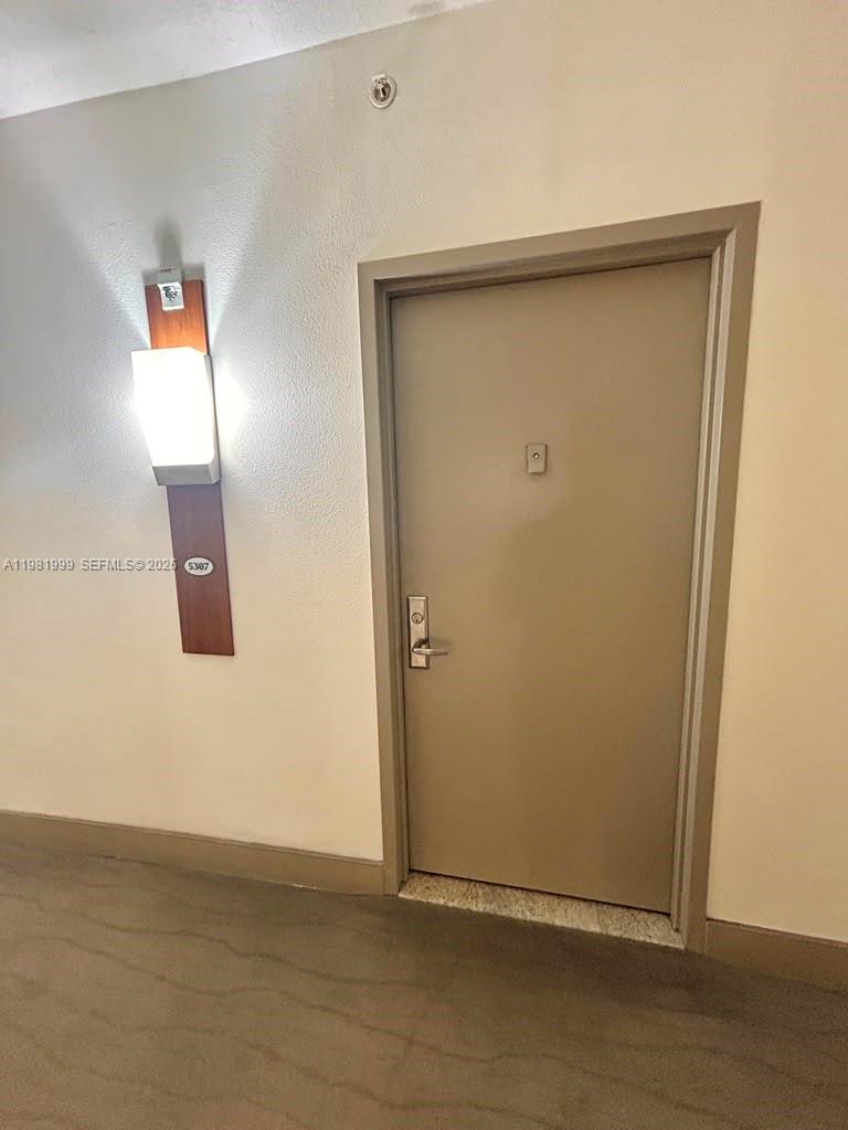 A hallway features a beige door with a peephole next to a wall-mounted light fixture — 1750 N Bayshore Dr # 5307, Miami FL 33132, MIAMI, FL