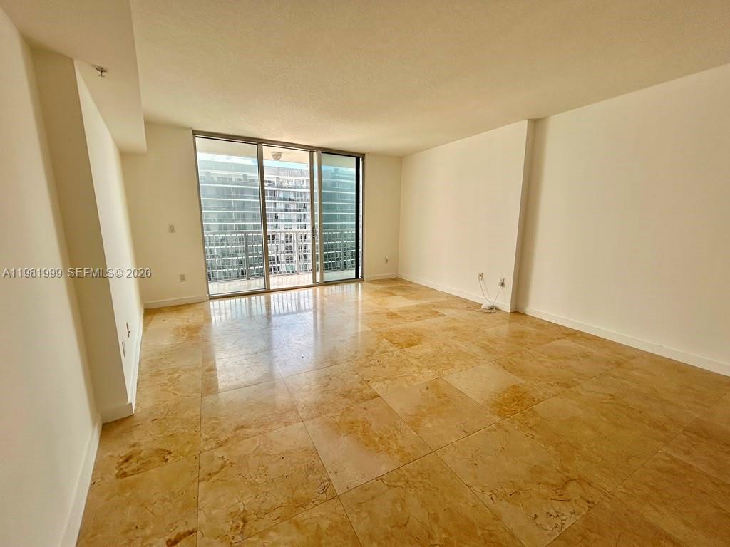An empty room features beige tile flooring, white walls, and a sliding glass door balcony — 1750 N Bayshore Dr # 5307, Miami FL 33132, MIAMI, FL