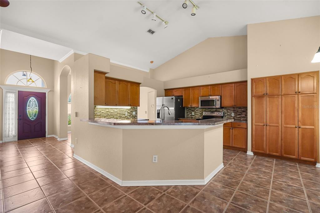 A kitchen with wood cabinets, a breakfast bar, and tile flooring opens to an entryway — 3806 OPAL CIRCLE, ST CLOUD, FL