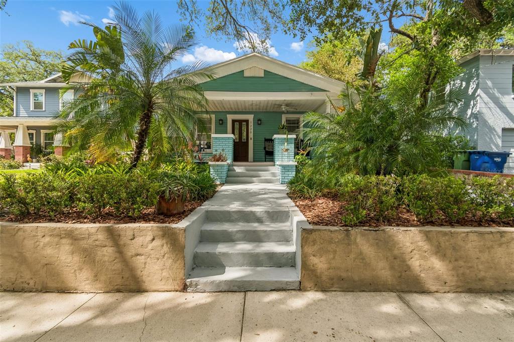 A teal bungalow with a front porch, palm trees, and a concrete retaining wall — 1220 E EMMA STREET, TAMPA, FL