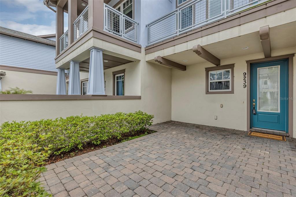 A paved patio leads to a blue front door of a multi-story residential building — 9239 DOHERTY PLACE, ORLANDO, FL