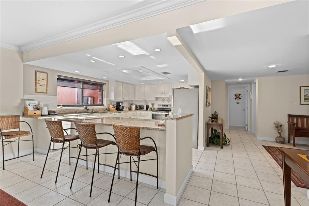 A kitchen features white cabinetry, granite countertops, a breakfast bar with stools, and tile flooring — 3230 SOUTHSHORE DRIVE UNIT 36B, PUNTA GORDA, FL