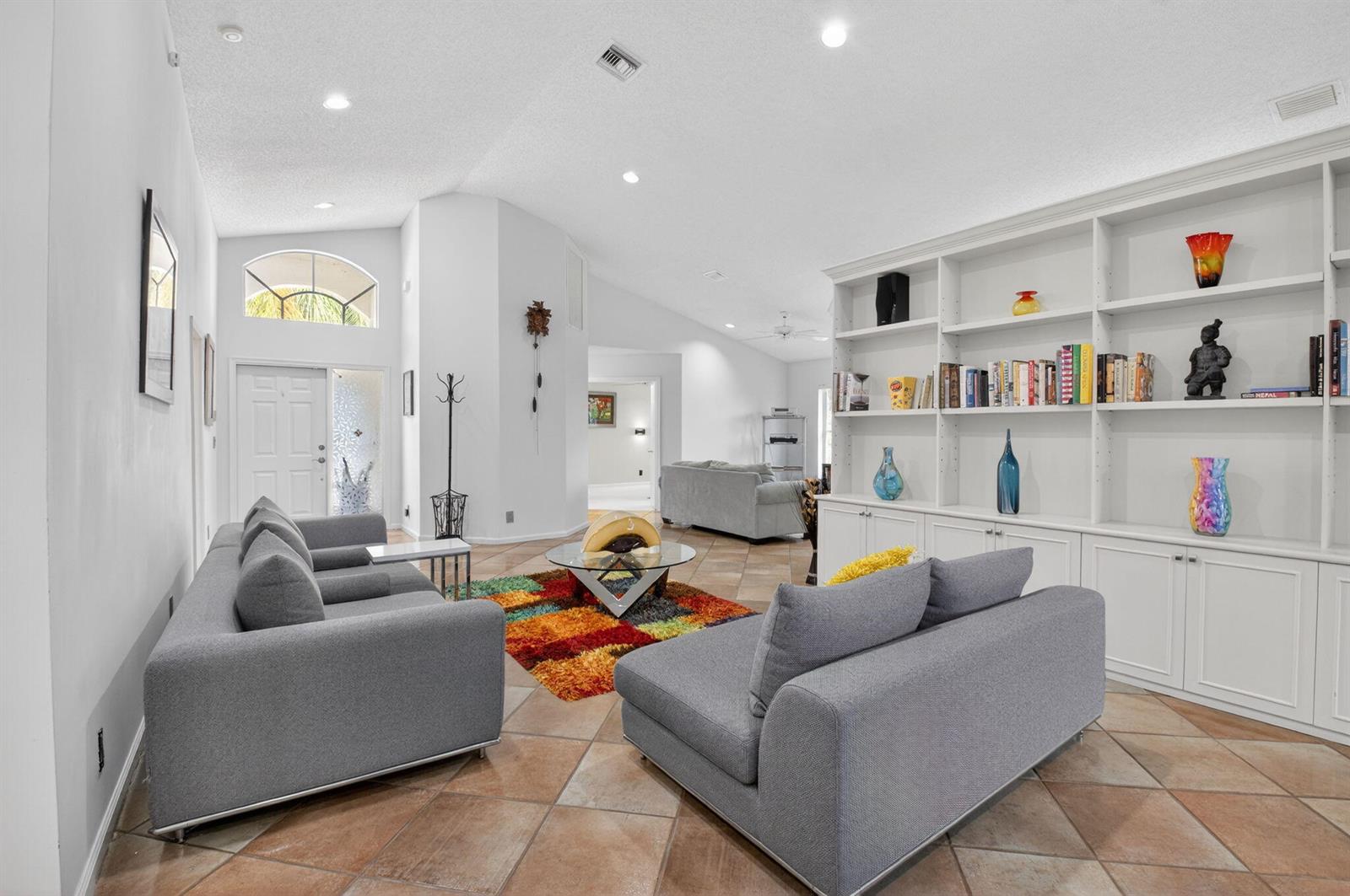 A living room features gray sofas, a colorful rug, and a large white built-in bookshelf — 11590 Creekside Drive, Boynton Beach FL 33437, BOYNTON BEACH, FL