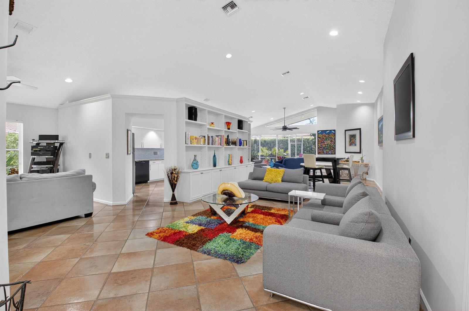 A spacious living room features tile floors, a large built-in bookshelf, and a colorful rug — 11590 Creekside Drive, Boynton Beach FL 33437, BOYNTON BEACH, FL