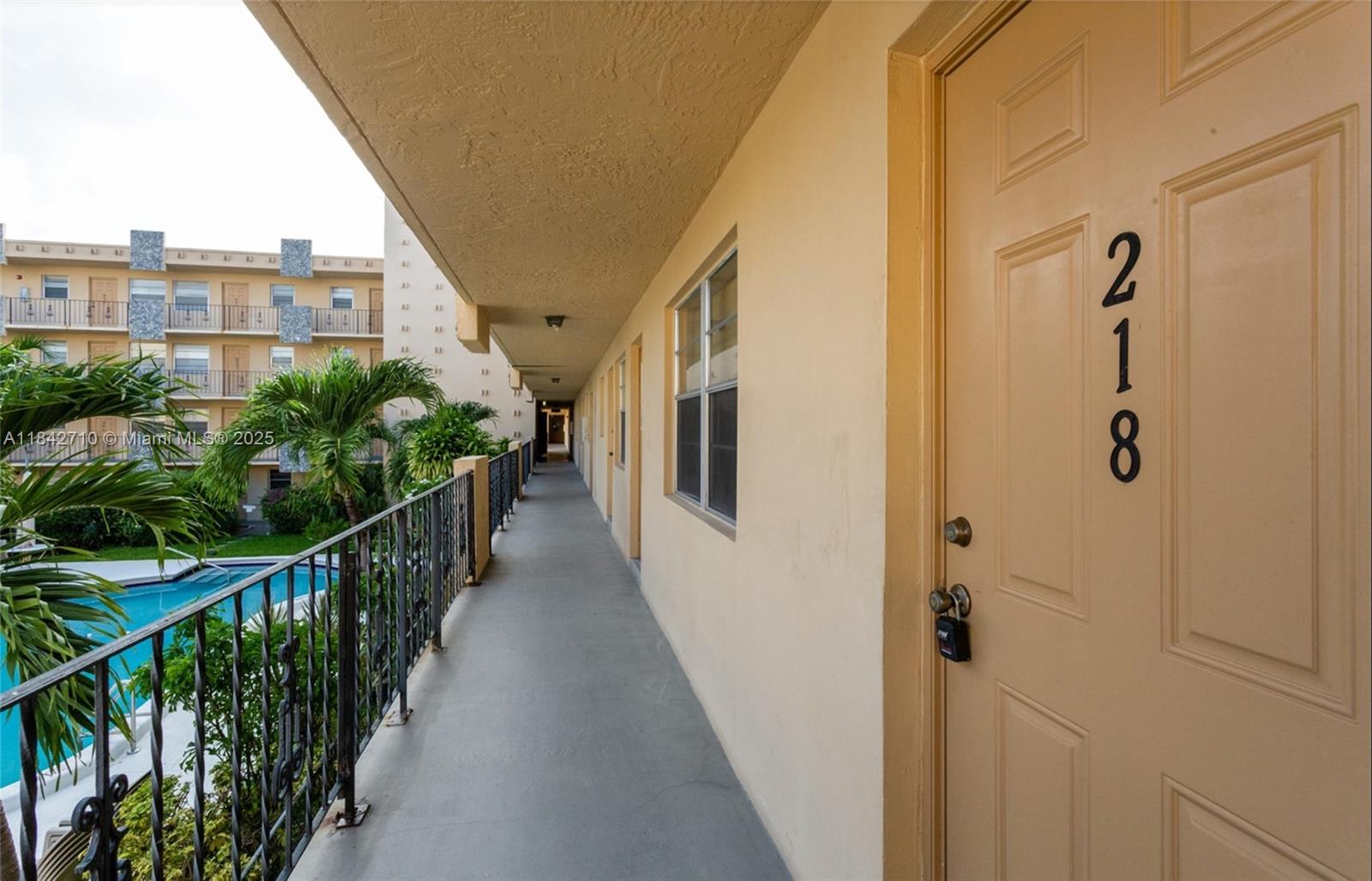 An exterior apartment walkway features a door numbered 218, a metal railing, and a pool — 2145 Pierce St # 218, Hollywood FL 33020, HOLLYWOOD, FL
