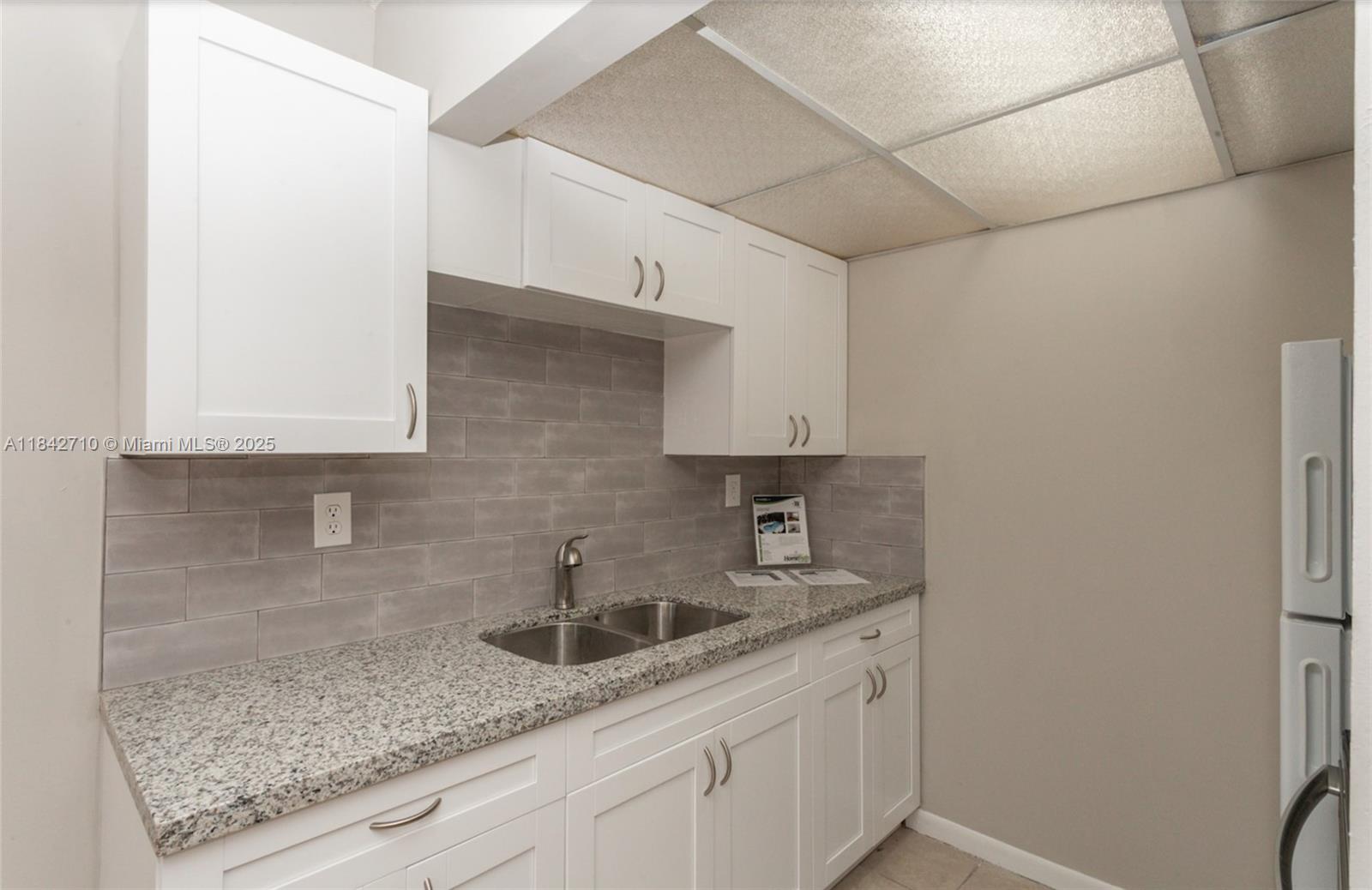 A kitchen features white cabinets, granite countertops, a double sink, and gray subway tile backsplash — 2145 Pierce St # 218, Hollywood FL 33020, HOLLYWOOD, FL