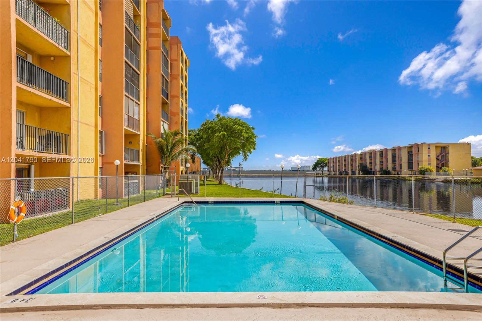 A rectangular swimming pool sits in front of a multi-story apartment building and a lake — 4805 NW 7th St # 15, Miami FL 33126, MIAMI, FL