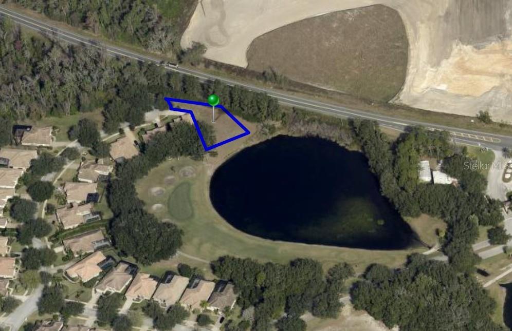 An aerial view shows a vacant lot outlined in blue next to a lake — 9901 SANTA BARBARA COURT, HOWEY IN THE HILLS, FL