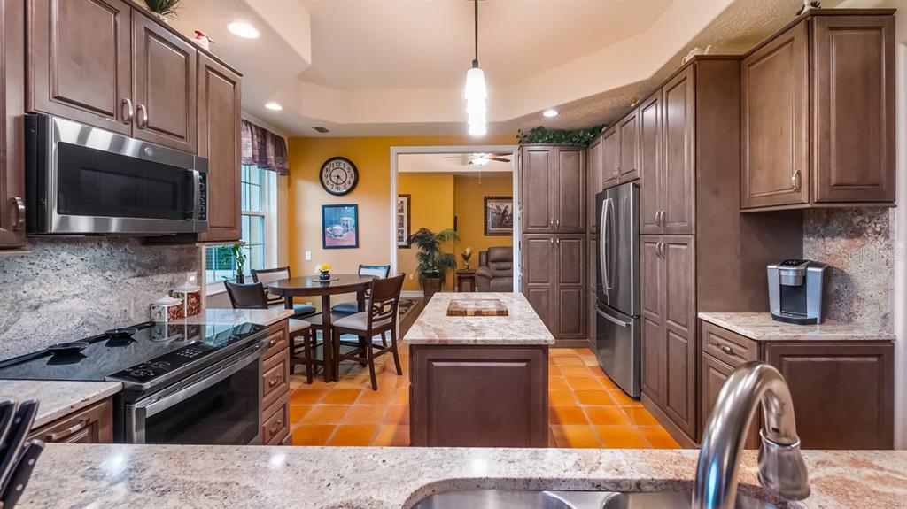 A kitchen features wood cabinets, stainless steel appliances, a granite-topped island, and orange tile flooring — 82 CAMINO REAL BOULEVARD UNIT 82, HOWEY IN THE HILLS, FL