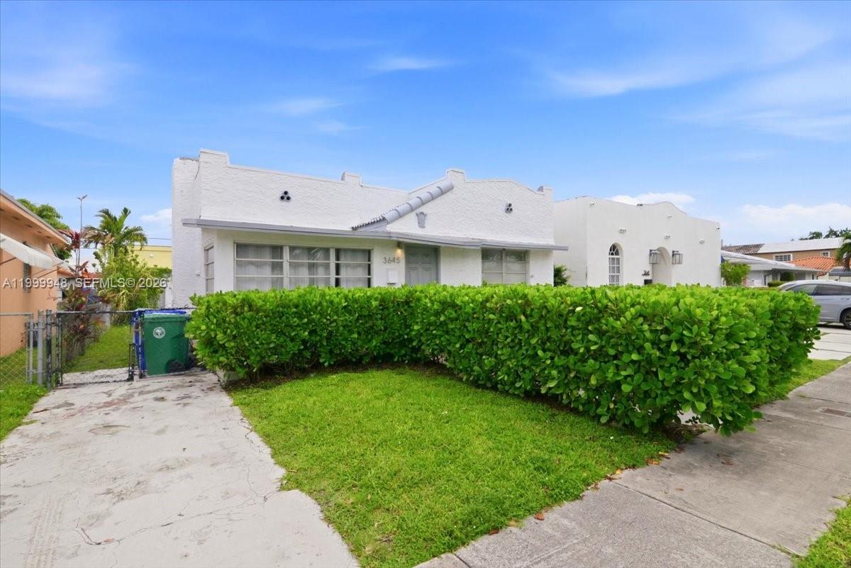 A white stucco house with a green hedge and a concrete driveway sits under blue skies — 3645 SW 25th Ter, Miami FL 33133, MIAMI, FL